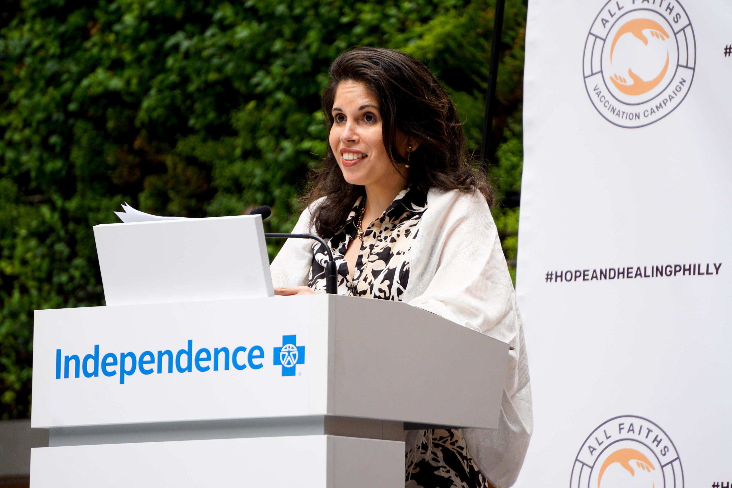 A woman speaking at a podium with the AFVC logo displayed repeatedly on a press conference backdop.